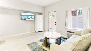 A spacious living room with a large TV, a white wardrobe, a round coffee table, and a sofa. - Siesta Key Village, Pool, Beach Access 4-min. Walk, 1bdr (Siesta Key)