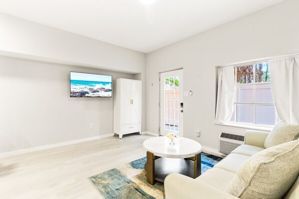 A spacious living room with a large TV, a white wardrobe, a round coffee table, and a sofa. - Siesta Key Village, Pool, Beach Access 4-min. Walk, 1bdr (Siesta Key)