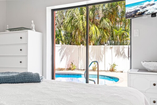 A bedroom with a bed, a dresser, and a view of a swimming pool and palm trees. - Siesta Key Village, Pool, Beach Access 4-min. Walk, 1bdr (Siesta Key)