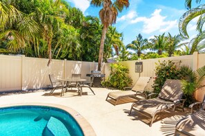 Un espace piscine aménagé avec des chaises longues, une table et un barbecue.