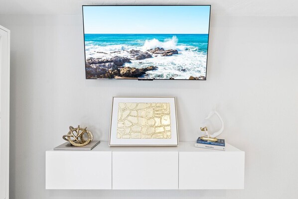 Un téléviseur à écran plat fixé au-dessus d’une console blanche, agrémenté d’une œuvre d’art encadrée et d’objets décoratifs.