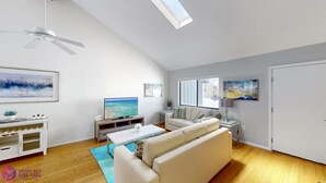 A spacious living room with a sofa, coffee table, TV, and artwork on the walls.