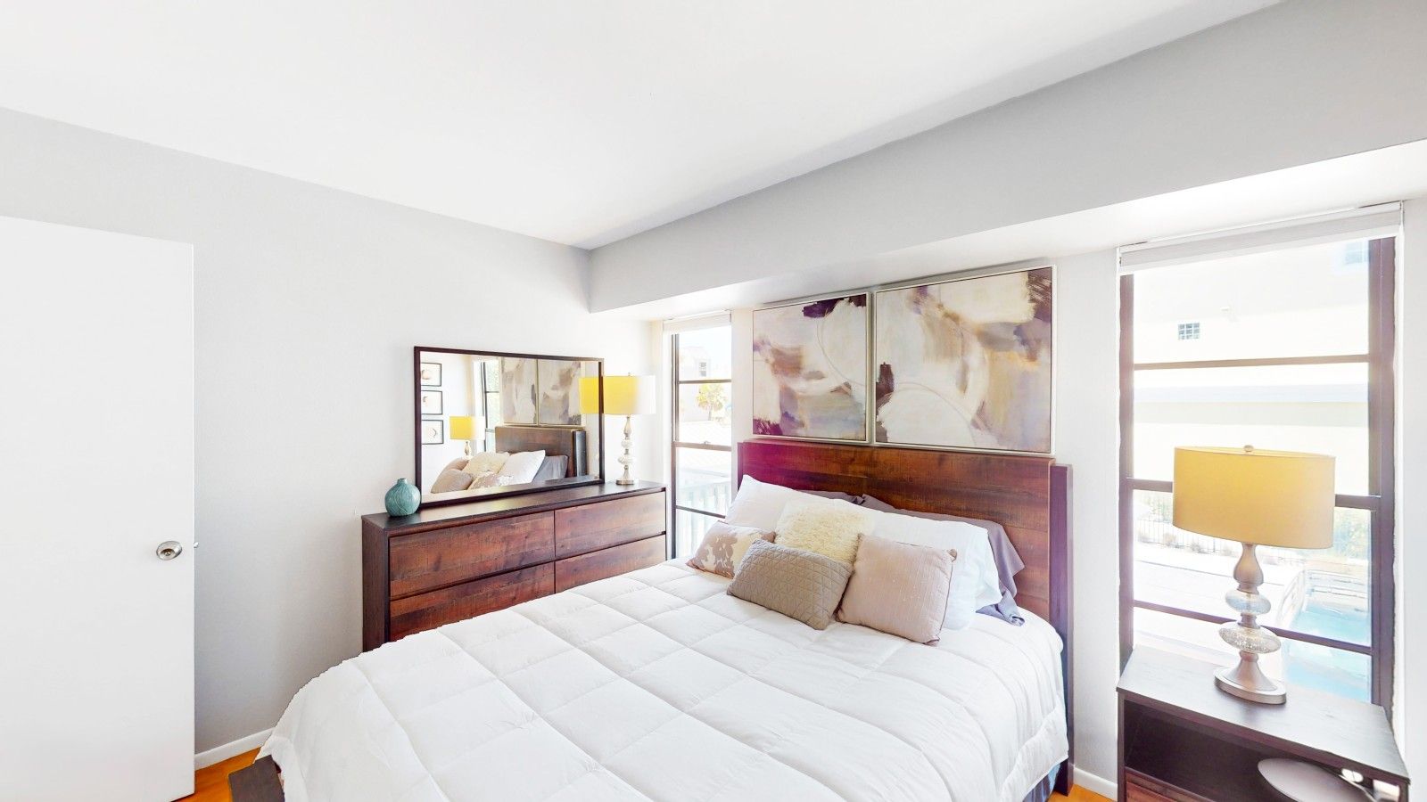 A bedroom with a bed, a dresser, a mirror, and a window with a view.