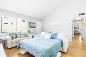 Ein Schlafzimmer mit einem großen Bett, einem Sofa, einem kleinen Tisch und einem Fenster mit Blick auf Gebäude.