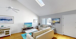 A spacious living room with a sofa, coffee table, TV, and artwork on the walls.
