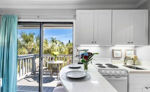A kitchen with a large window, a dining area with a table and chairs, and a view of palm trees outside.
