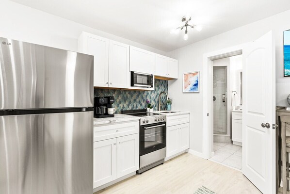 A modern kitchen with white cabinets, stainless steel appliances, a microwave, and a coffee maker. - Beach Rd, 300ft to Beach Access & 500ft to Siesta Key Village, 1bdr (Siesta Key)