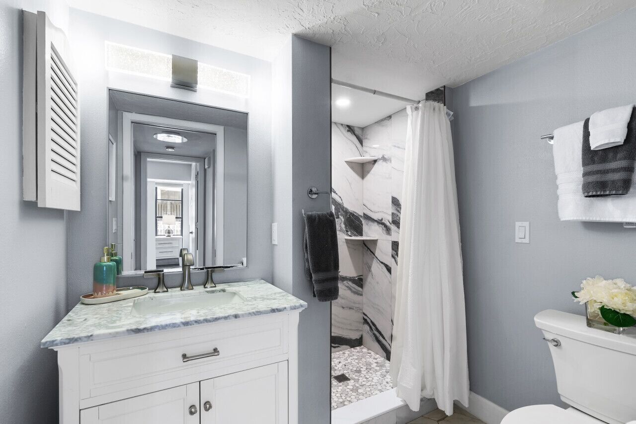 A modern bathroom with a white vanity, a glass shower enclosure, and a toilet with a flower vase.