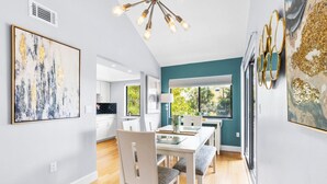 Un espace repas moderne avec une table blanche, des chaises à revêtement gris et une table avec un plateau en verre. Un luminaire est suspendu au plafond au-dessus de la table.