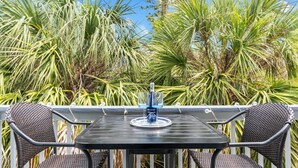 Une table avec une bouteille et un verre, entourée de chaises en osier, le tout placé devant un décor de grandes plantes vertes.