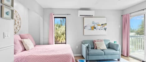 A bedroom with a bed, a sofa, a large window, and a ceiling fan.
