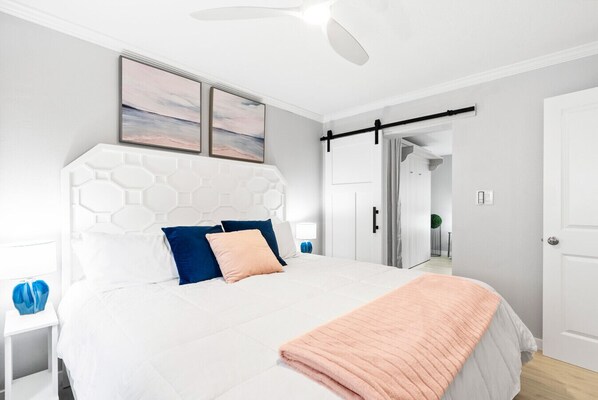 A modern bedroom with a white bed, blue and peach pillows, a white headboard, and a ceiling fan. - Beach Rd, 300ft to Beach Access & 500ft to Siesta Key Village, 1bdr (Siesta Key)