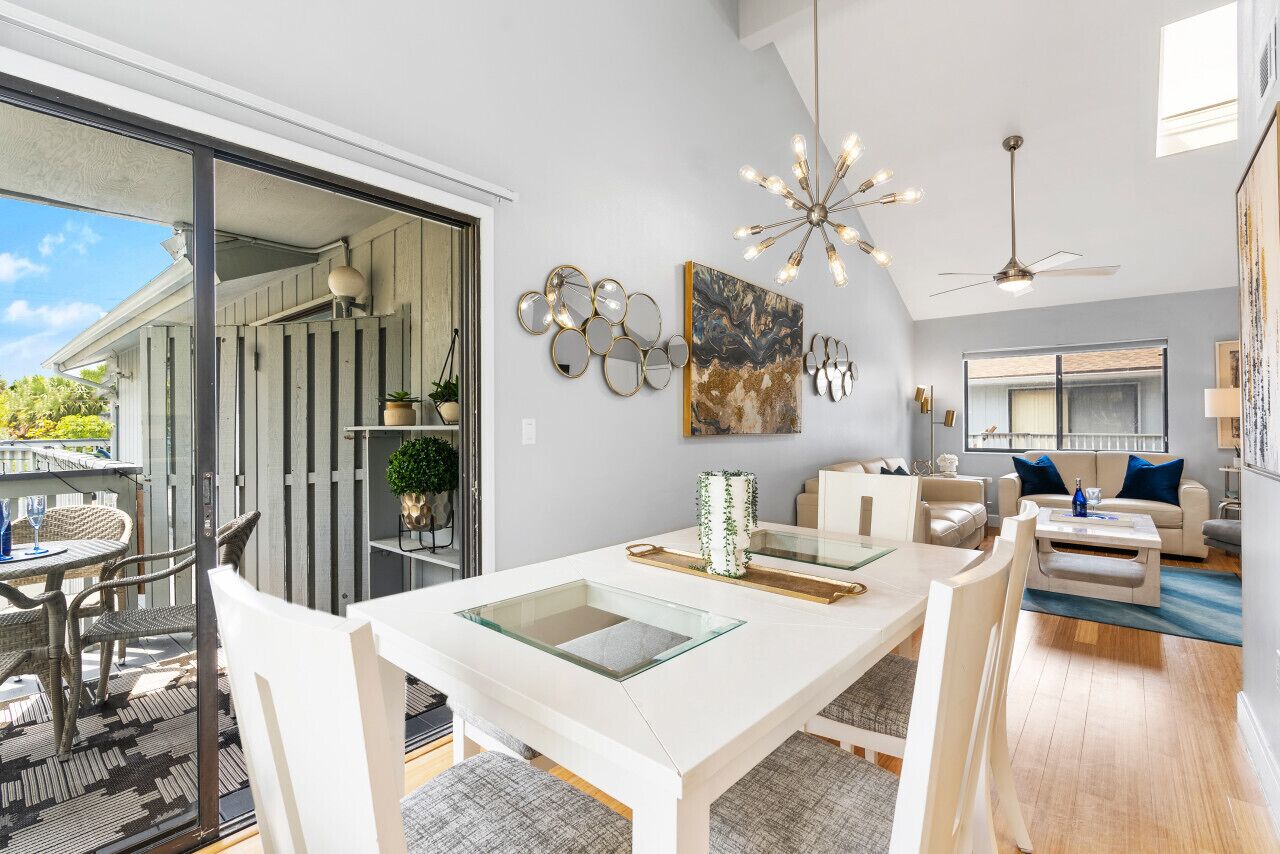 A modern living room with a glass dining table, white sofas, and a ceiling fan.