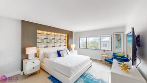 Un dormitorio moderno con una cama grande, mesitas de noche, televisión y vistas a la ciudad.