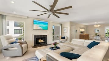 Una sala de estar moderna con un sofá modular grande, un sillón blanco, una chimenea y un ventilador de techo.