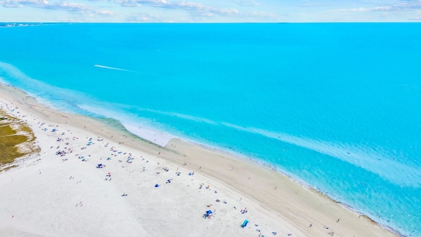 Vue aérienne d’une plage aux eaux turquoise et limpides et au rivage sablonneux.