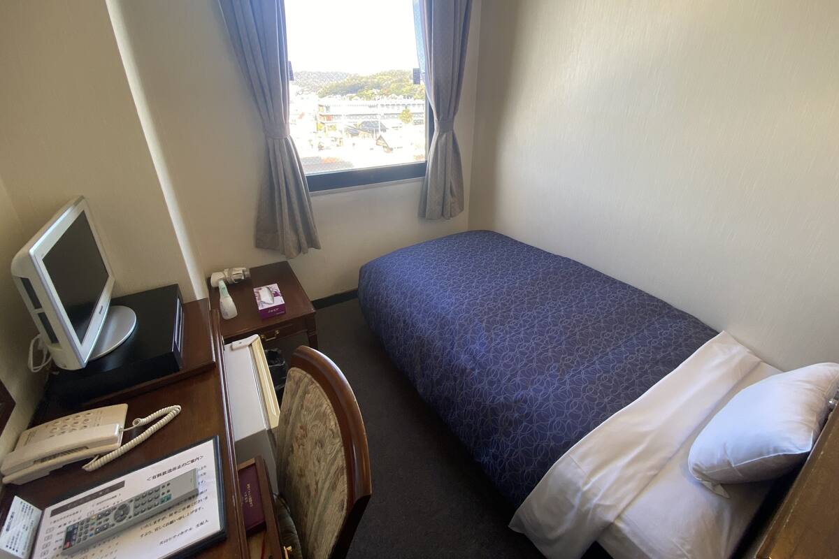 Une chambre d’hôtel avec un lit, un bureau doté d’un écran d’ordinateur, un téléphone et une fenêtre avec des rideaux.