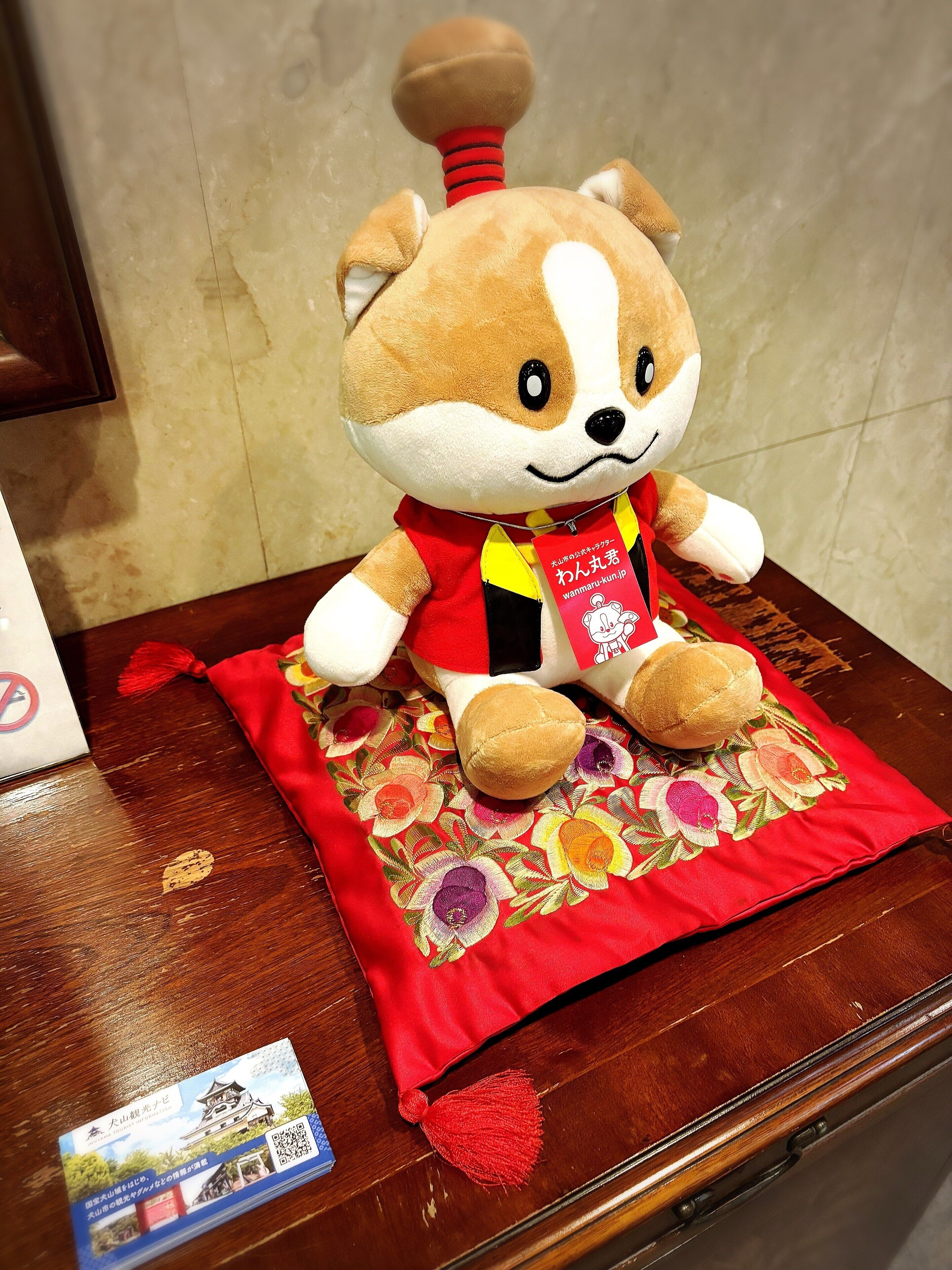 A plush toy on a wooden table with a red cloth and a business card.