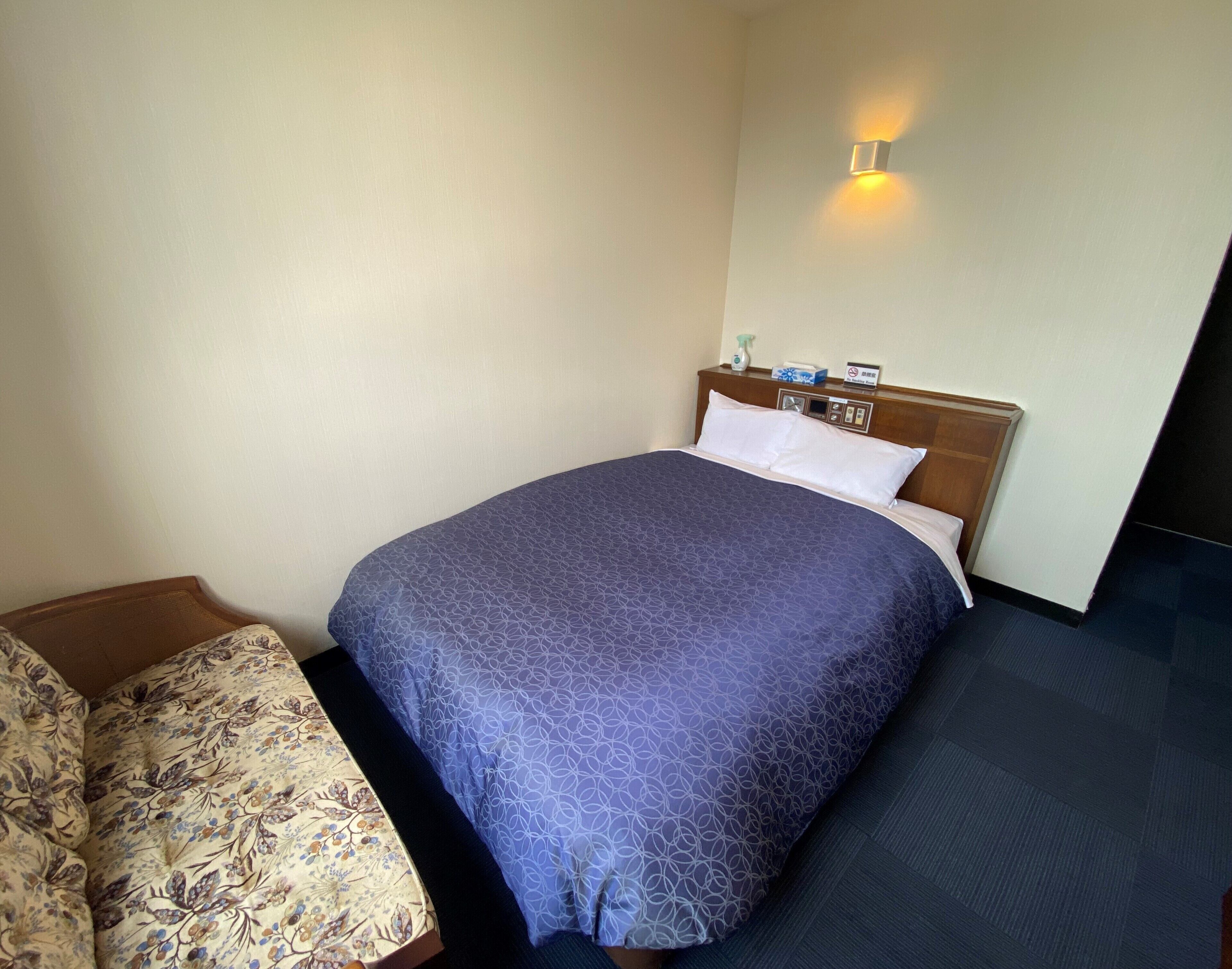 A hotel room with a neatly made bed, a bedside table with a lamp, and a wall-mounted light fixture.