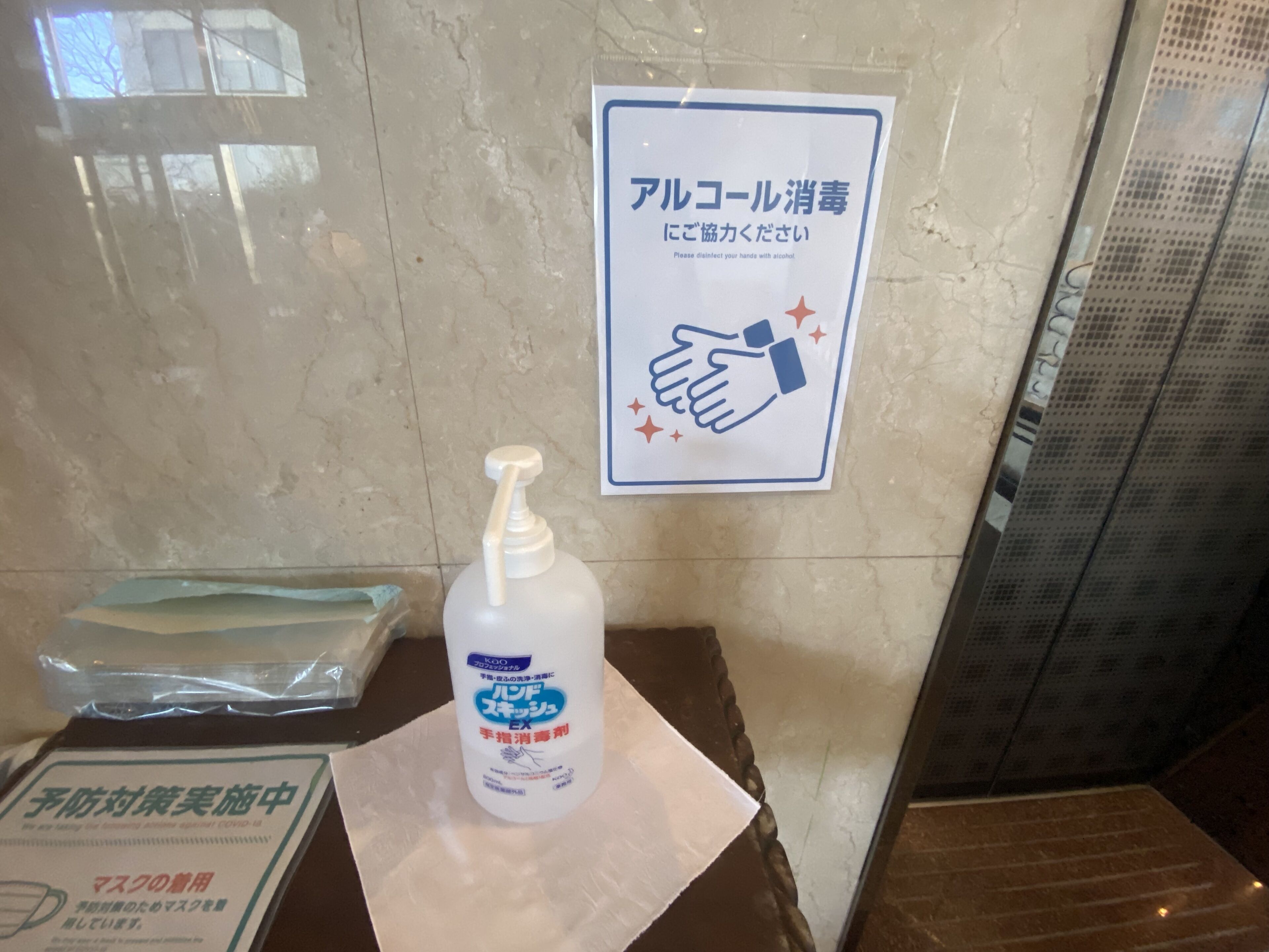 Una botella de gel hidroalcohólico sobre una mesa con un letrero que indica desinfectar las manos con alcohol.