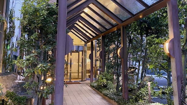 Un edificio moderno con una galería techada, puertas de vidrio y un jardín arbolado.