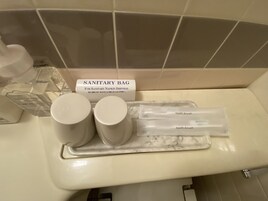 Zona de lavamanos con dispensador de bolsas sanitarias, dos vasos y dos cepillos de dientes.