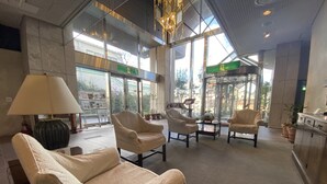 Un vestíbulo amplio con asientos cómodos, una mesa de recepción y grandes ventanales que ofrecen vistas al exterior.