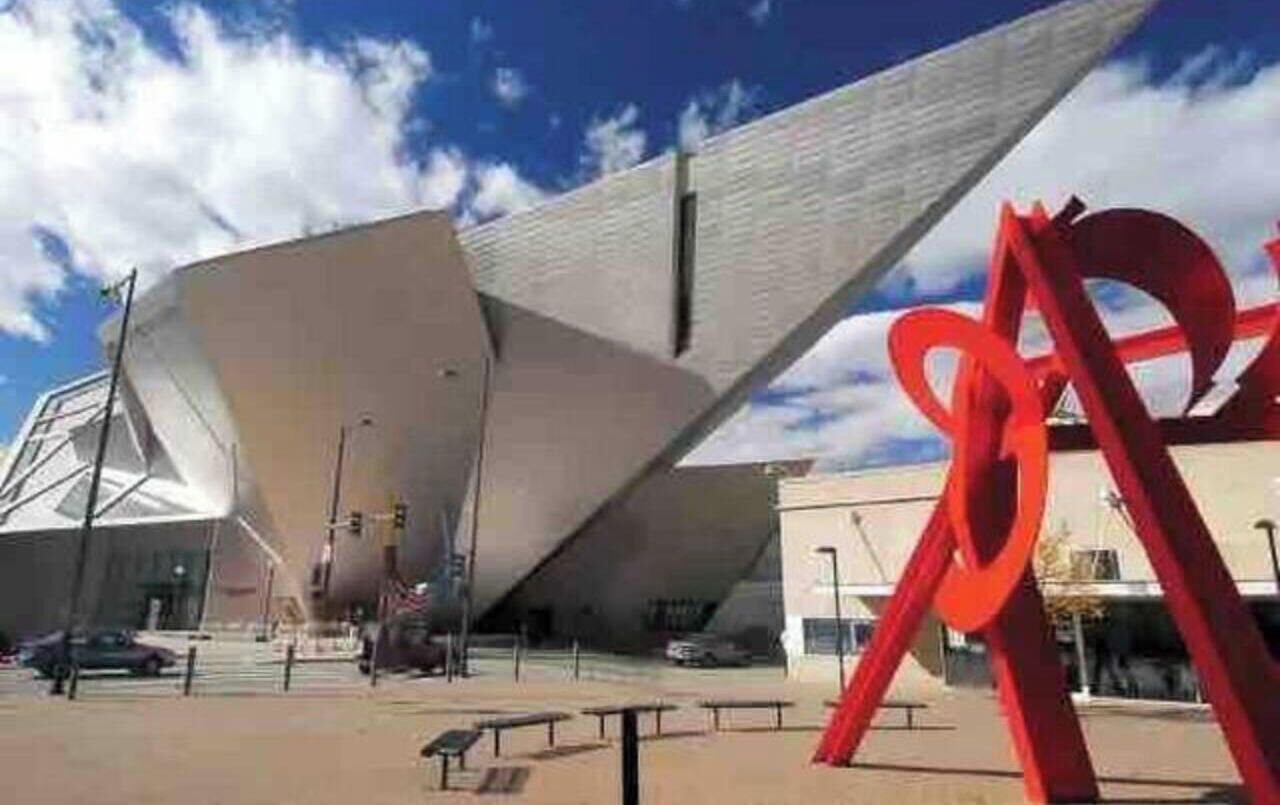 Un bâtiment moderne au design angulaire original, une sculpture rouge imposante et un ciel d’un bleu éclatant.