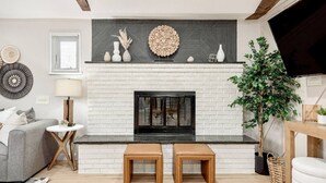 A living room with a fireplace, a sofa, two wooden stools, a side table, and a potted plant.