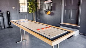 Ein Shuffleboardtisch in einem Raum mit grauer Wand, einem Fenster und einer Pflanze.