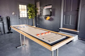 Taula de joc de bitlles en una habitació amb paret gris, finestra i una planta.