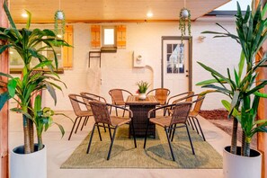 A dining area with a round table and wicker chairs, surrounded by potted plants.