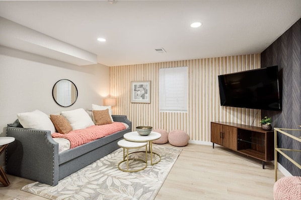 A modern living room with a grey sofa, a round coffee table, and a flat-screen TV mounted on the wall.