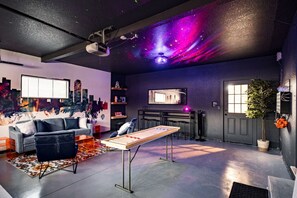 A modern living room with a cityscape mural, a gaming table, and a projector on the ceiling.