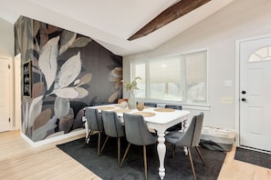 A dining area with a white table, grey chairs, and a large floral mural on the wall.