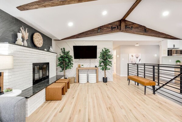 A modern living space with a fireplace, wooden flooring, a staircase, and a flat-screen TV.