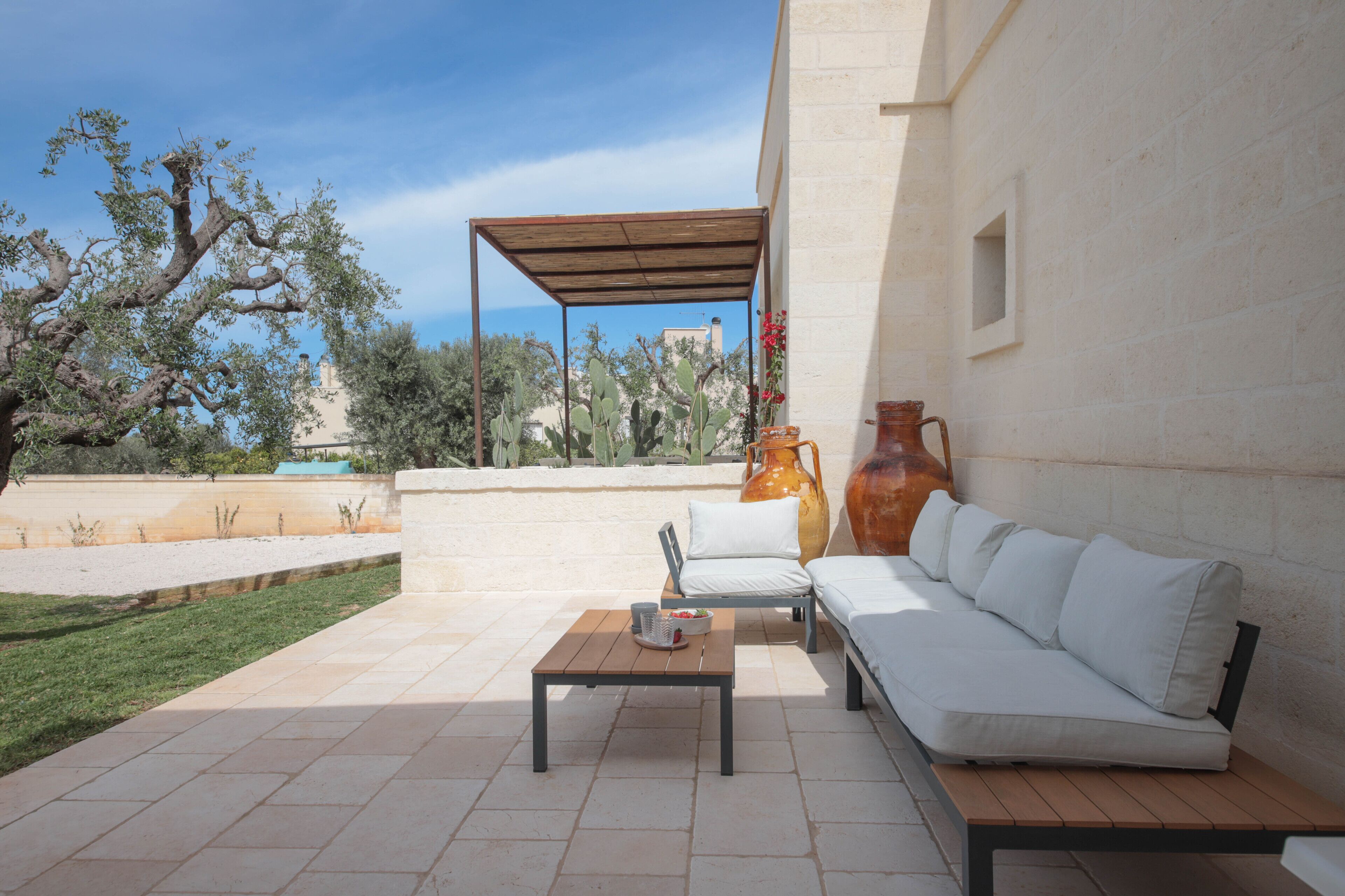 Eine Terrasse im Freien mit einem weißen Sofa, einem Holztisch und zwei großen Vasen.