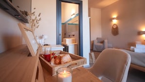 Ein gemütliches Zimmer mit Holztisch, Kerze, Tablett mit Gebäck und Getränken sowie einem Bett im Hintergrund.