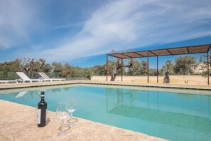Une piscine agrémentée d’une pergola, de chaises longues et d’une bouteille de vin posée sur le bord.
