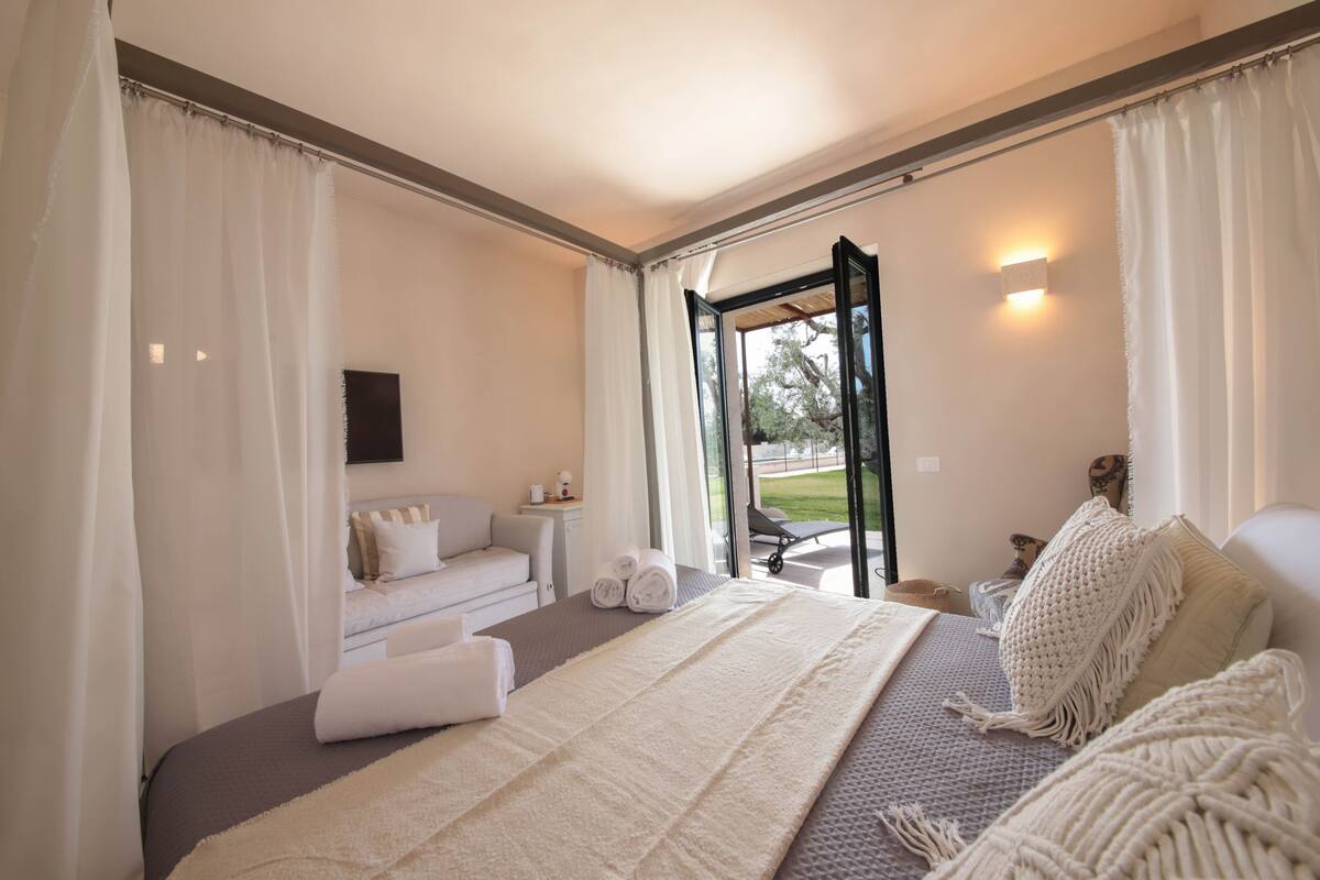 Une chambre d’hôtel moderne avec un grand lit, un canapé, une petite table avec une lampe et une vue sur l’extérieur.