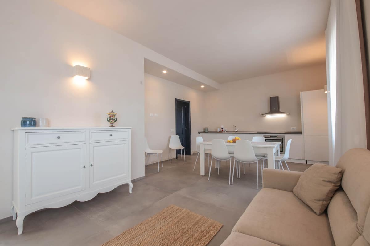 Un salon moderne avec un canapé beige et un coin repas comprenant des chaises blanches et une table.