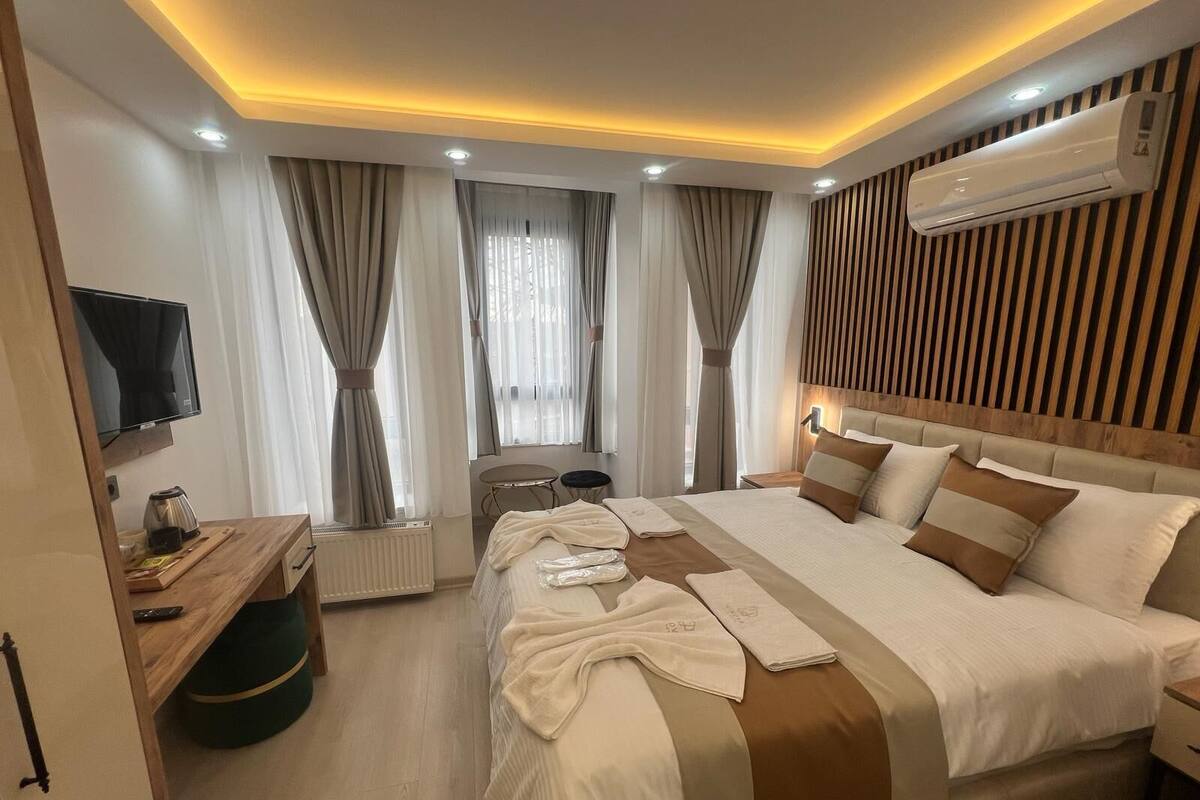 A modern hotel room with a large bed, a TV, a desk with a kettle, and a radiator.