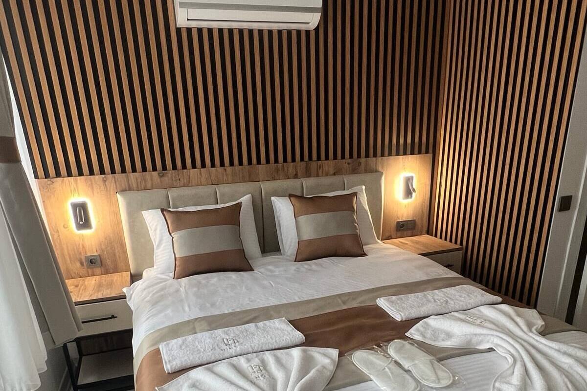 A modern bedroom with a wooden slat headboard, a central air conditioning unit, and a neatly made bed with white linens and decorative pillows.