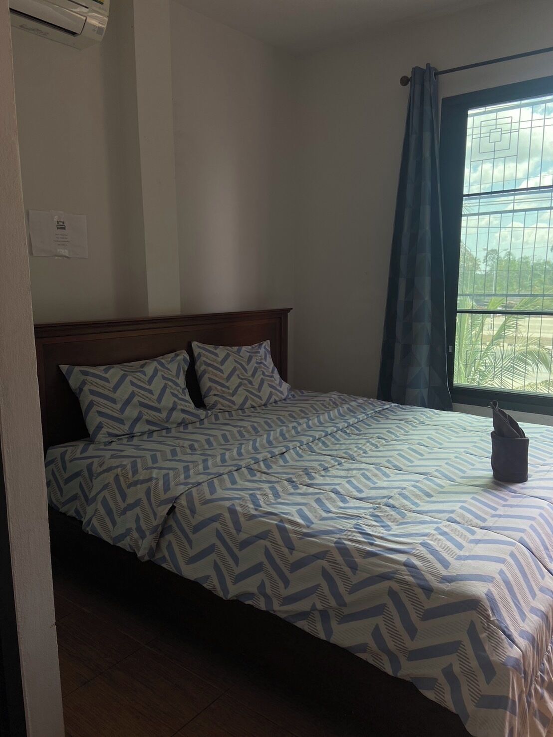 A bedroom with a bed, a window with curtains, and an air conditioning unit.