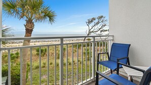 A balcony with a view of the ocean, a palm tree, and a chair. - Villas By The Sea #184 - Oceanfront (Jekyll Island)