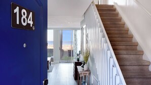 A modern interior with a blue door marked '184', a staircase, and a view to the outside. - Villas By The Sea #184 - Oceanfront (Jekyll Island)