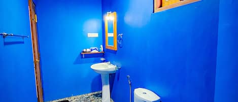 A bathroom with blue walls, a white sink, a toilet, and a window with a view of greenery.