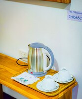Una tetera de acero inoxidable sobre una mesa de madera, con un cartel con la contraseña de WiFi arriba.