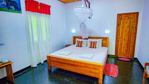 A bedroom with a wooden bed, a ceiling fan, a wall-mounted light, a door, and a small table. - Sunbird's Home  (Udawalawa)