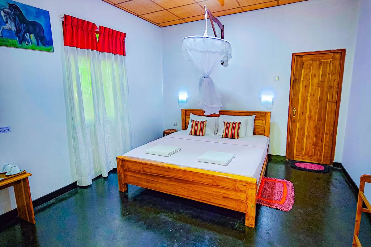 A bedroom with a wooden bed, a ceiling fan, a wall-mounted light, a door, and a small table.